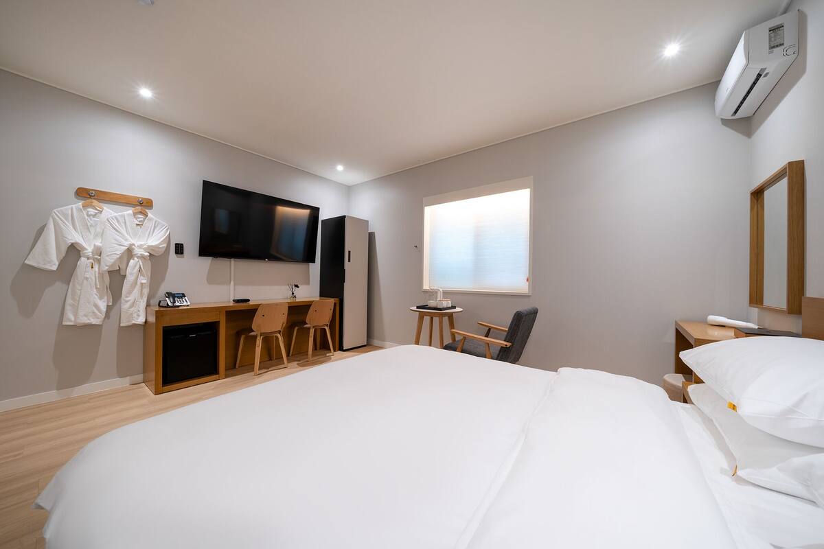 A hotel room with a large bed, a desk with a chair, a TV, and a window with blinds.