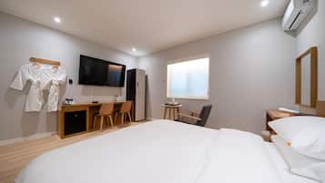 Una habitació d'hotel amb un llit gran, un escriptori amb una cadira, un televisor i una finestra amb persianes.