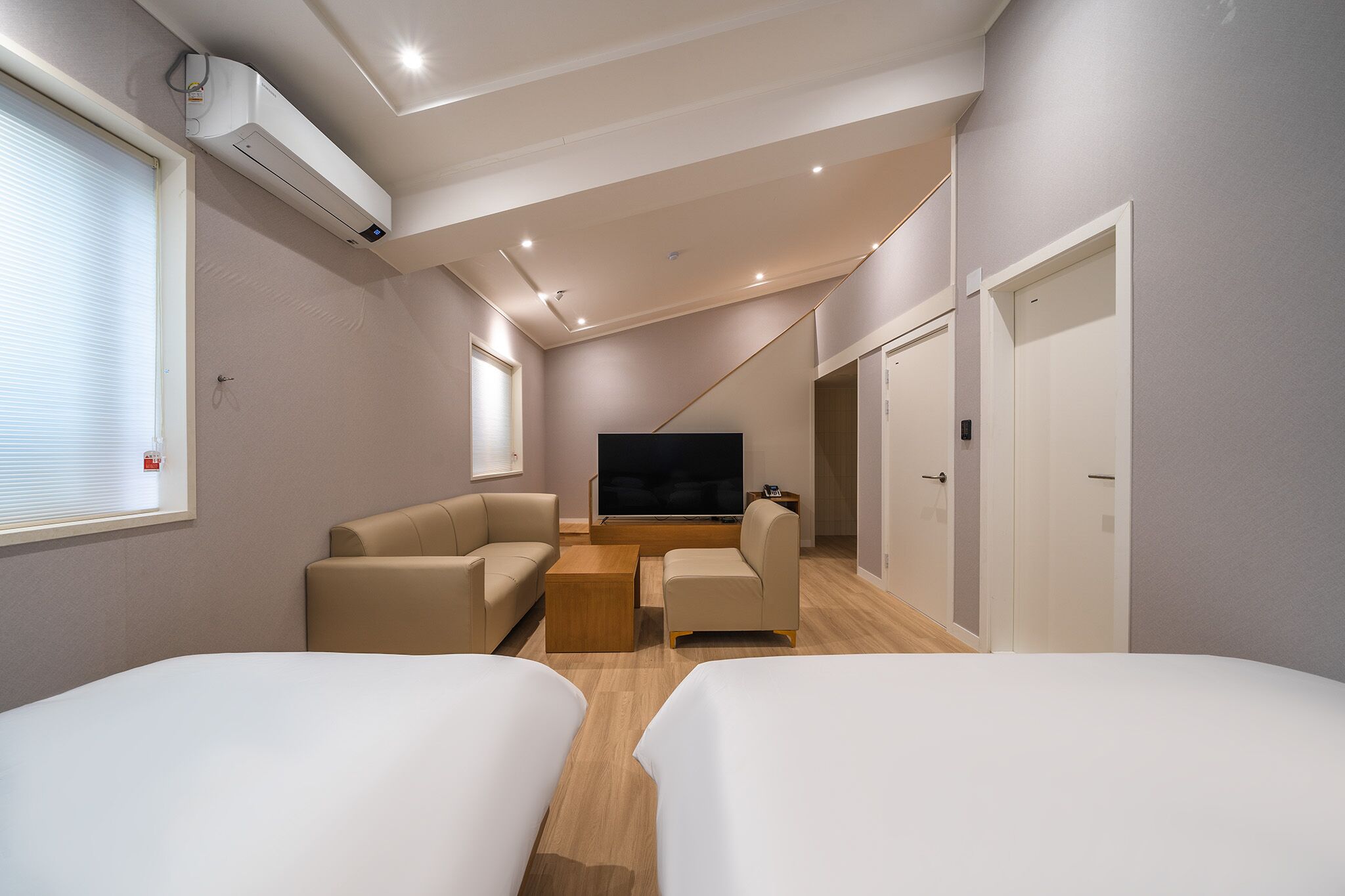 Una habitación de hotel moderna con dos camas, un televisor de pantalla plana, un sofá y una mesa de centro.
