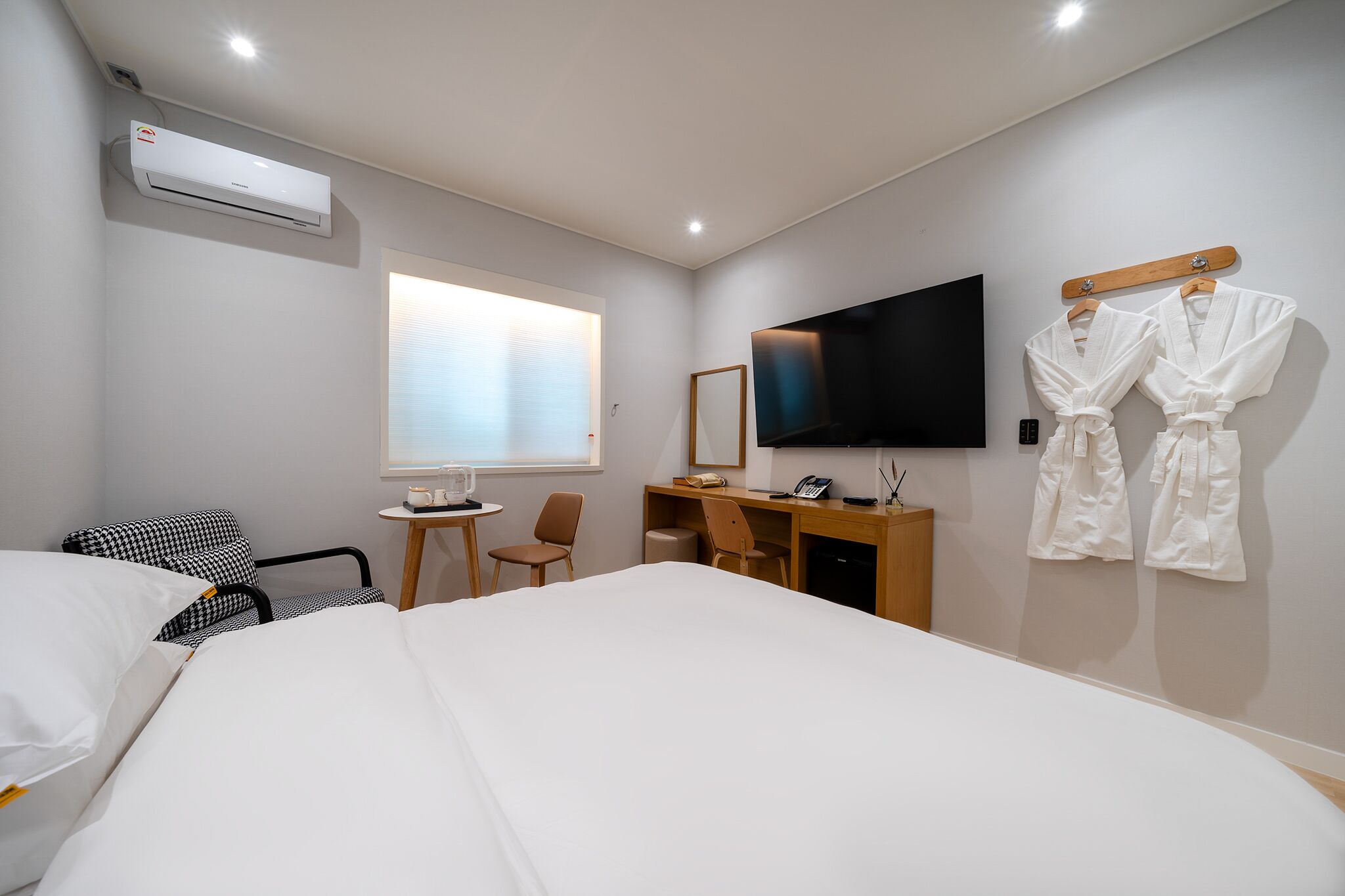 A hotel room with a bed, a desk, a TV, a mirror, and two robes on a rack.