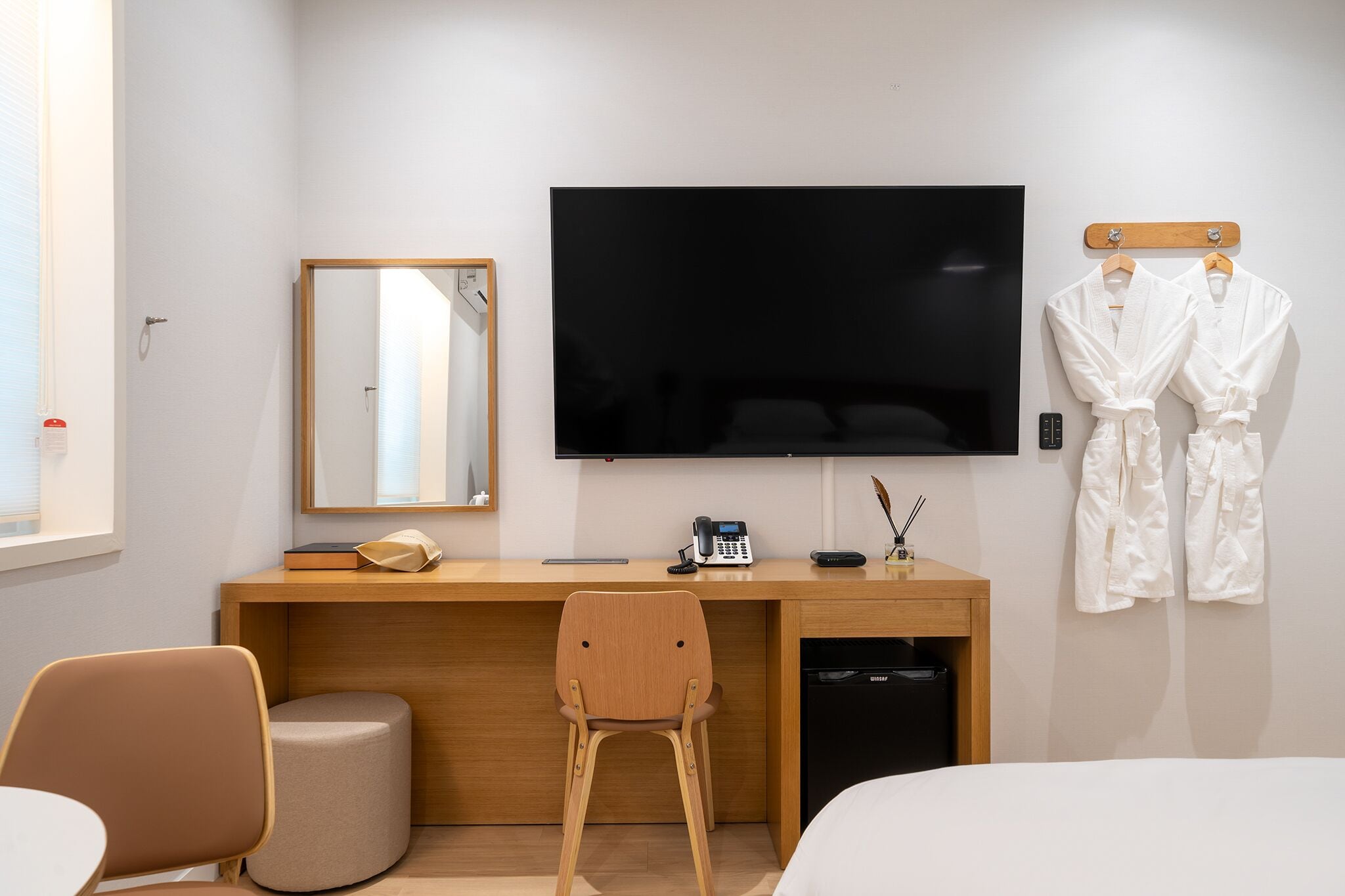Une chambre d’hôtel moderne équipée d’un bureau en bois, d’un téléviseur à écran plat, d’un miroir, d’un téléphone et d’un porte-peignoir.