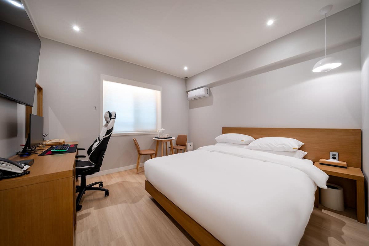 A hotel room with a bed, desk, chair, and a small table with a chair.
