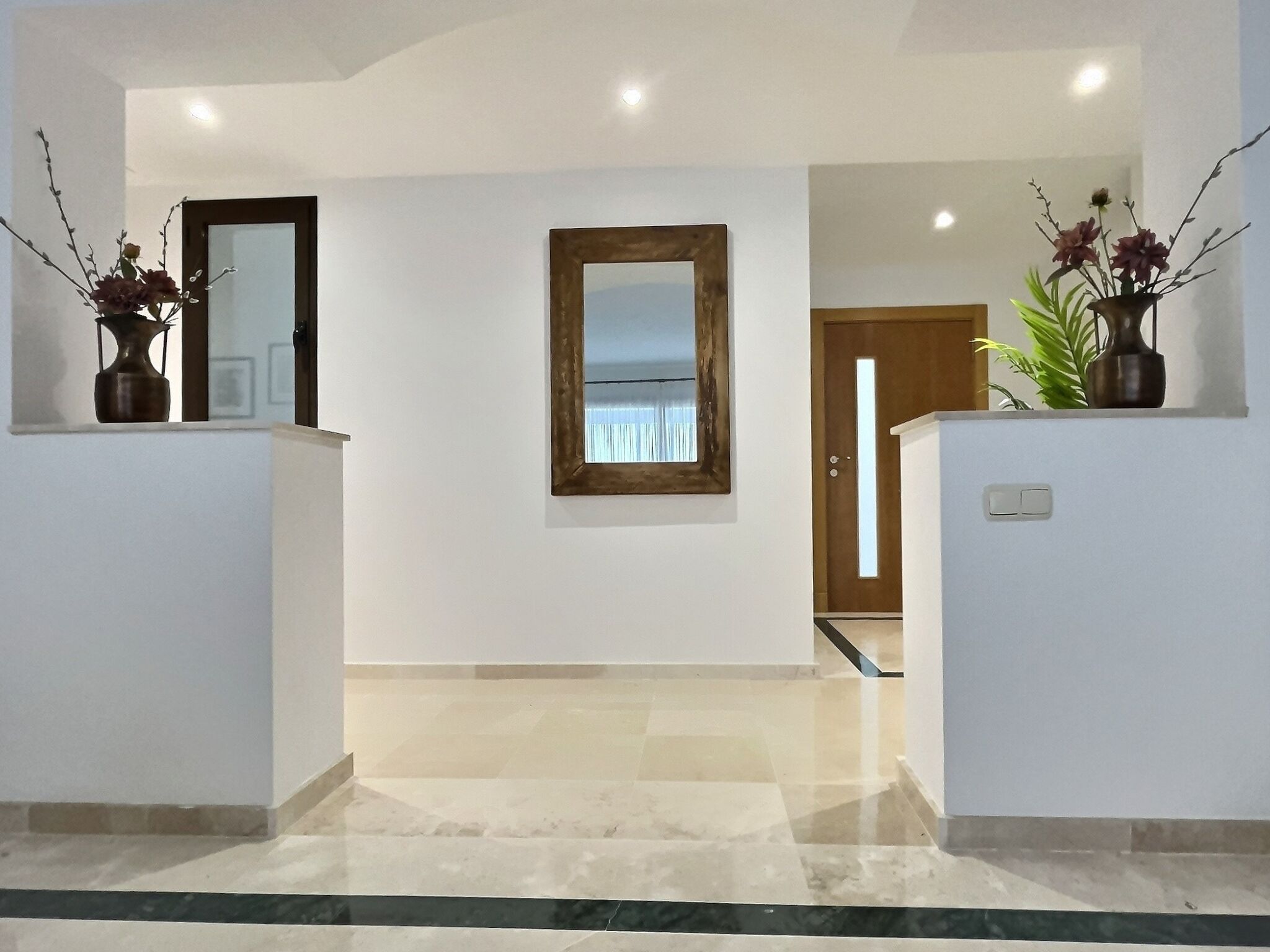 A hallway with a marble floor, a wooden-framed mirror, and a door leading to another room.