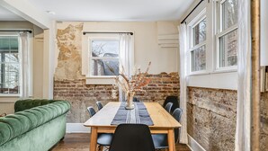 Ein Essbereich mit Holztisch, schwarzen Stühlen, einer grünen Couch und einer Ziegelwand.