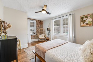 Ein Schlafzimmer mit einem großen Bett, einem Deckenventilator, einer Ziegelwand und einem Fenster mit Vorhängen.