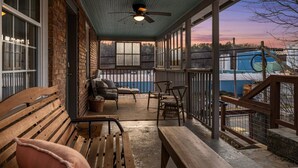 Eine überdachte Veranda mit hölzernen Bänken und Stühlen, einem Deckenventilator und großen Fenstern mit Blick auf die Umgebung.