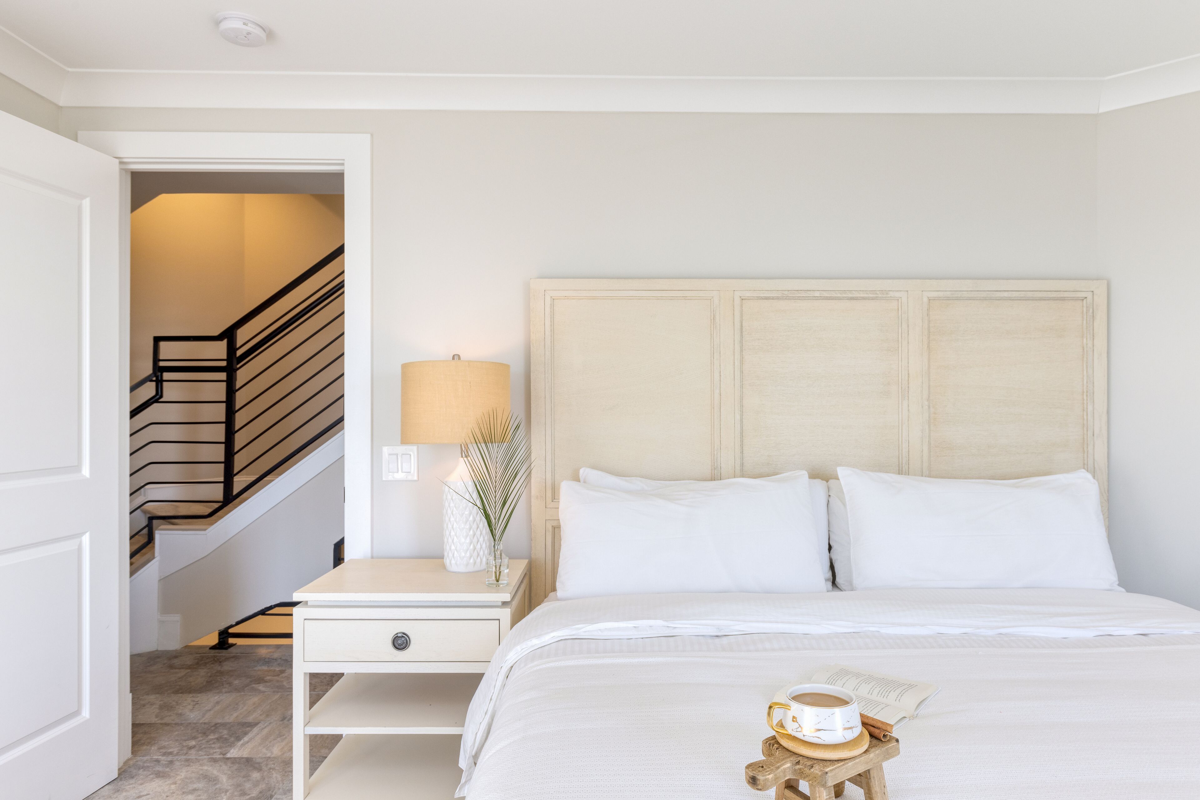 A bedroom with a bed, a nightstand, a lamp, and a cup of coffee on the nightstand.