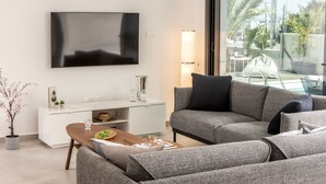 A modern living room with a flat-screen TV, a sofa, a coffee table, and a dining area with a white cabinet. - Protaras By the Bay Villa 32 (Paralimni)