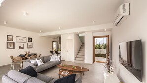 A modern living room with a sofa, coffee table, and TV. There is a staircase leading to another level. - Protaras By the Bay Villa 32 (Paralimni)