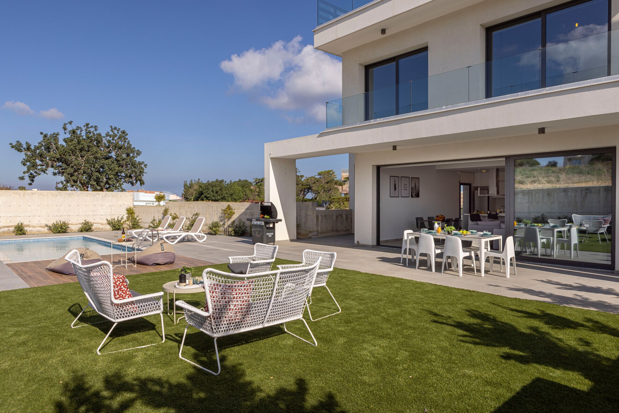 Eine moderne Außenpatio mit Pool, weißen Korbmöbeln und einer Essecke mit weißen Stühlen und Tischen.