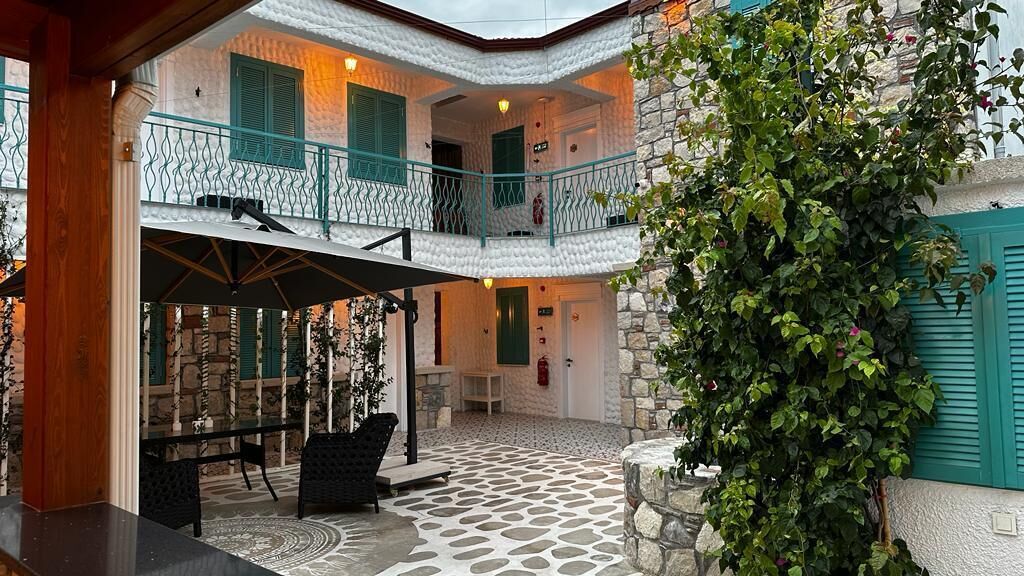 A courtyard with a stone floor, a table with chairs, and a balcony with green shutters.
