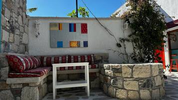 A stone bench with a white table in front, a colorful wall art piece, and a stone wall.