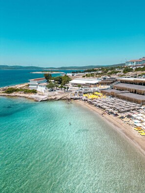 A coastal area with a beach, clear water, and wind turbines in the background. - Lotus City Siğacık Boutique Otel  (Seferihisar)