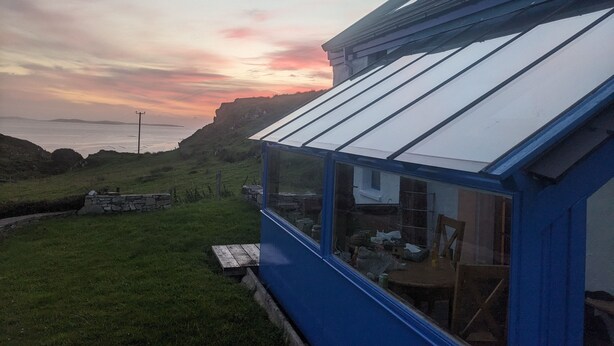 Une maison située sur la côte, avec une façade bleue et une grande véranda en verre.