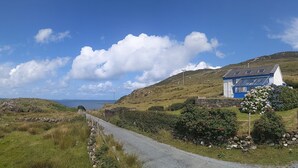 Un paysage rural avec un mur de pierres, une route étroite et une petite maison avec un toit bleu et des murs blancs.