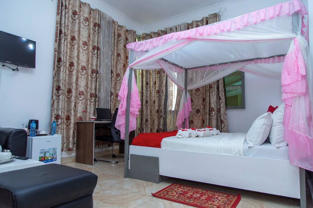Une chambre à coucher avec un lit à baldaquin, un bureau avec une chaise, une télévision et un petit réfrigérateur.