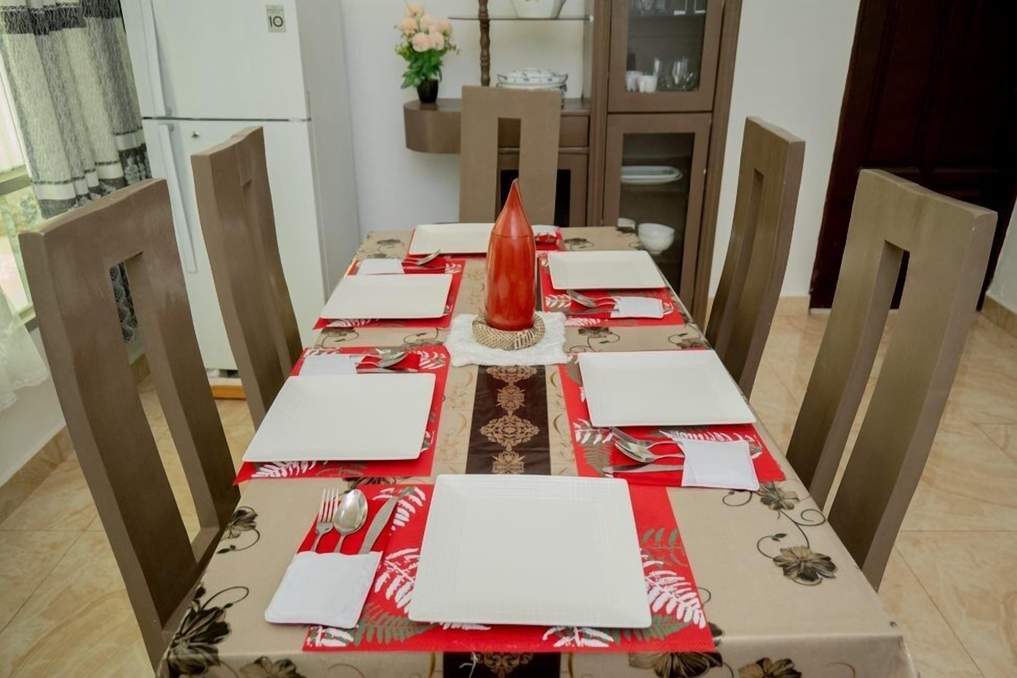 A dining table set for six with red napkins, white plates, and silverware.