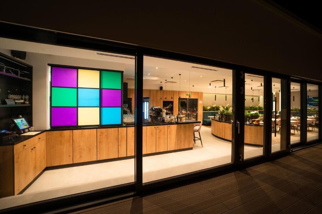 Una zona de bar moderna con un panel de luces colorido, armarios de madera y un espacio de estar con mesas y sillas.