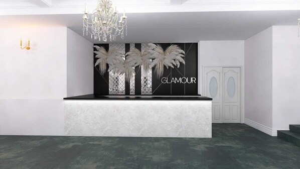 Zona de recepción con mostrador de mármol, candelabro y pared decorada con palmeras y la palabra “GLAMOUR”.