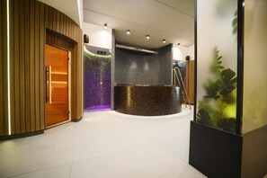 Un área de recepción moderna con un mostrador de madera, una pared de piedra con vegetación y un mostrador de recepción negro.