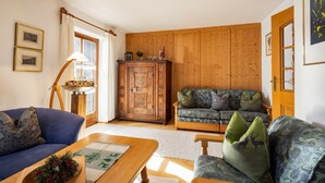 Een gezellige woonkamer met een blauwe bank, een houten salontafel en een gestreept fauteuil. In de achtergrond staat een houten kast en een groene bank.