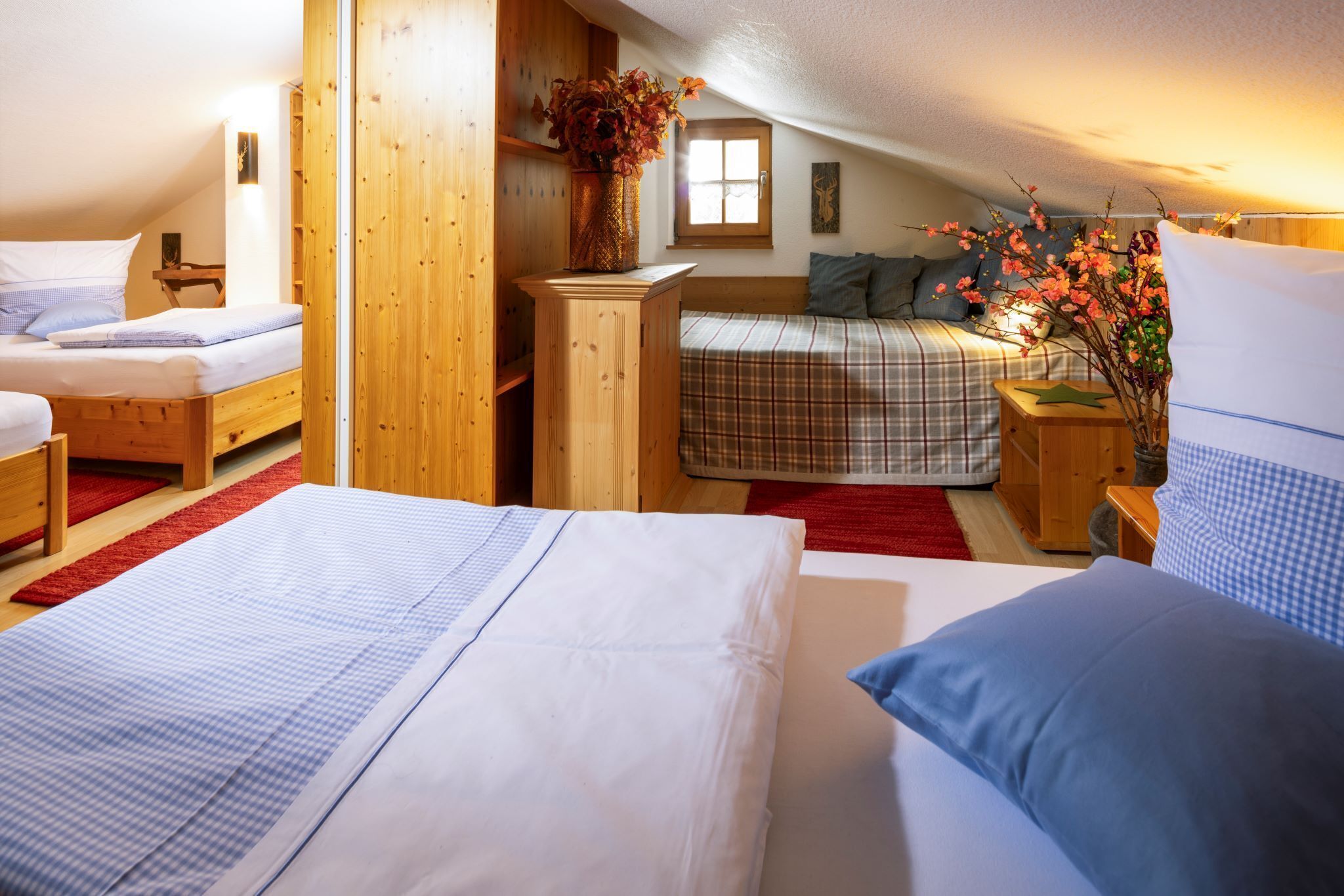Een gezellige slaapkamer onder de dakpannen met twee bedden, een houten dressoir, een vaas met bloemen en een raam.