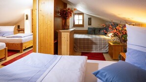 Een gezellige slaapkamer onder de dakpannen met twee bedden, een houten dressoir, een vaas met bloemen en een raam.