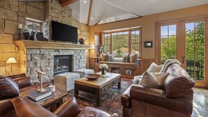 Una sala de estar con chimenea de piedra, mobiliario de cuero y grandes ventanales con vistas.
