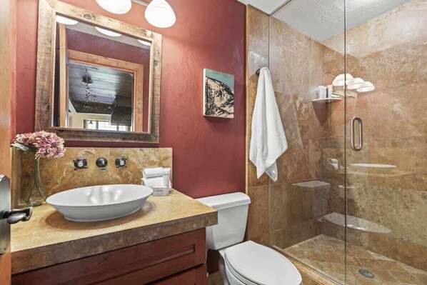 A bathroom with a large oval sink, a toilet, a glass-enclosed shower, and a mirror with a wooden frame.