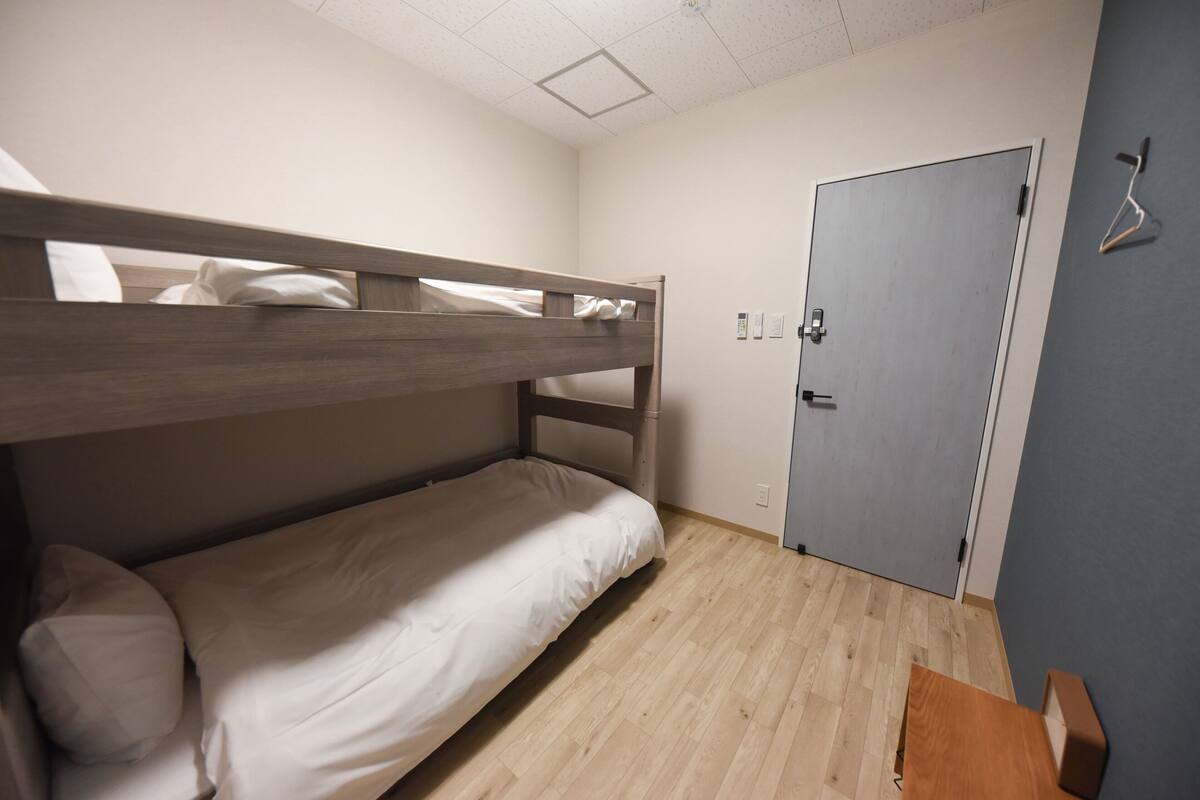 Une chambre avec un lit superposé, une porte et un porte-manteau fixé au mur.