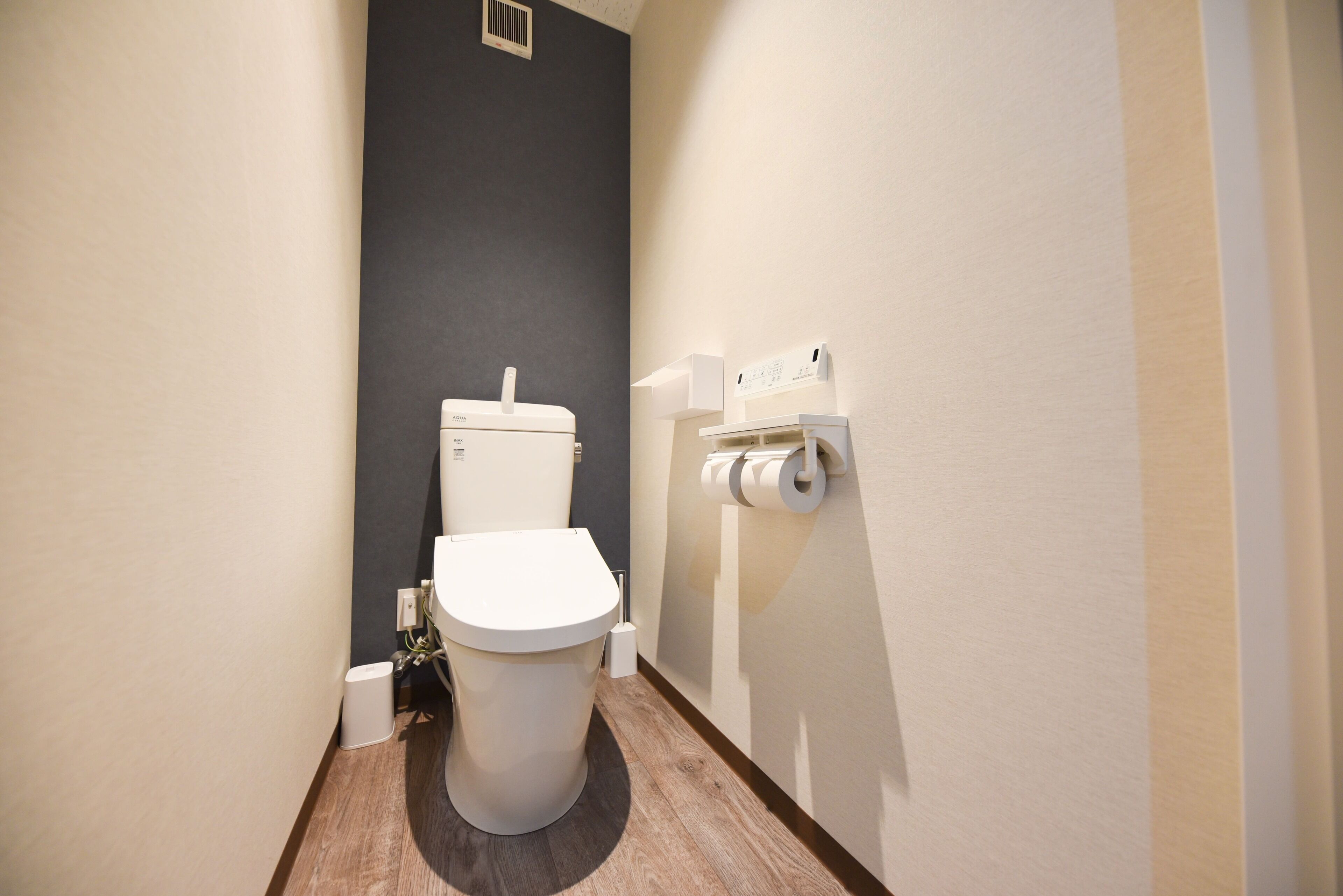 A small, modern bathroom with a white toilet, a dark accent wall, and a toilet paper holder on the wall.