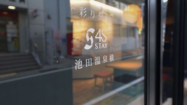 Une fenêtre d’hôtel avec une enseigne indiquant « 4S STAY » et du texte en japonais.