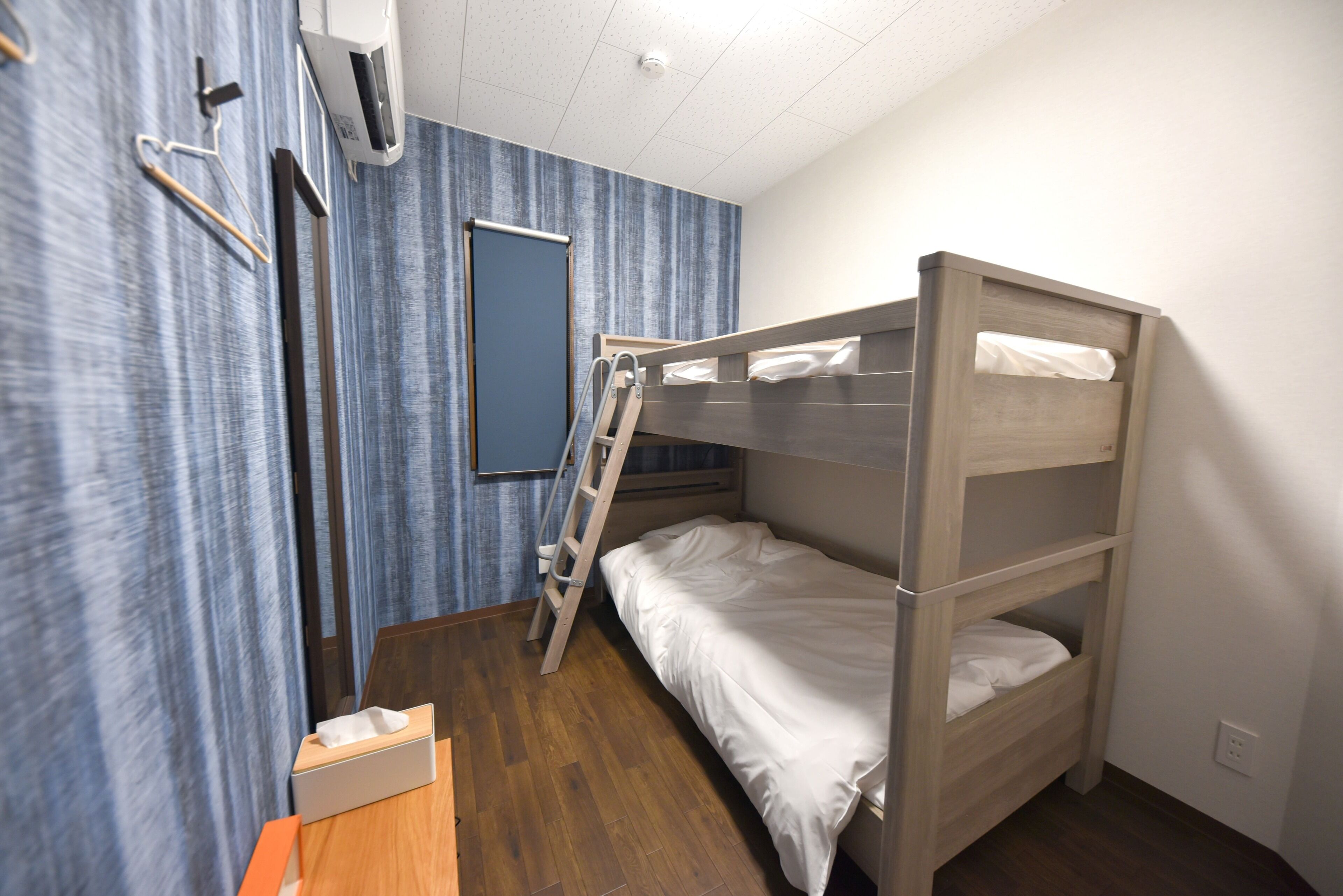 A bunk bed room with a wooden ladder, a small table, and a wall-mounted air conditioner.