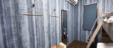 A modern hotel room with a wooden floor, a bunk bed, a wooden desk with a clock and tissues, a mirror, and a wardrobe with a sliding door.