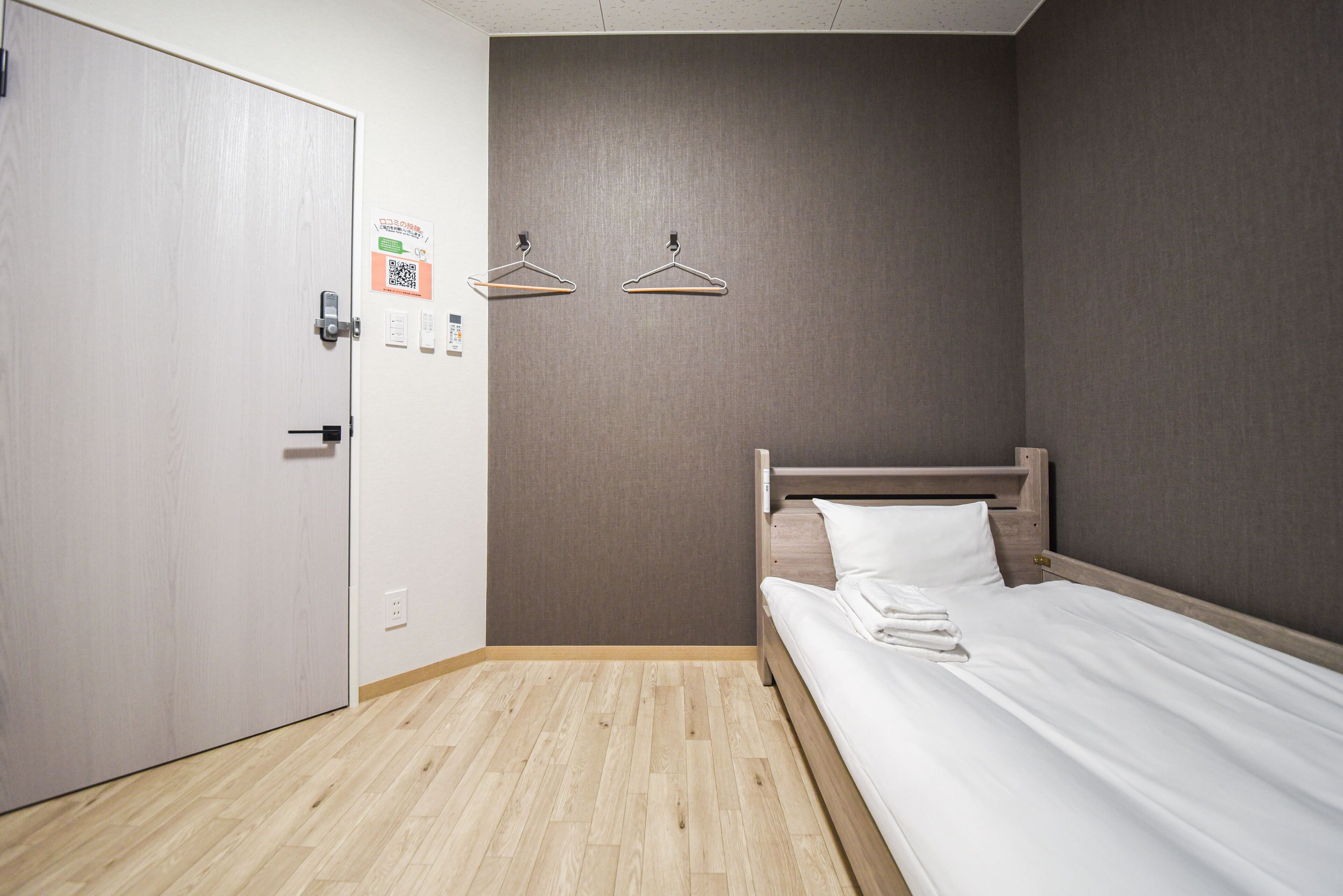 Habitación de hotel con piso de madera, cama con ropa blanca, cabecera de madera y dos colgadores de pared.