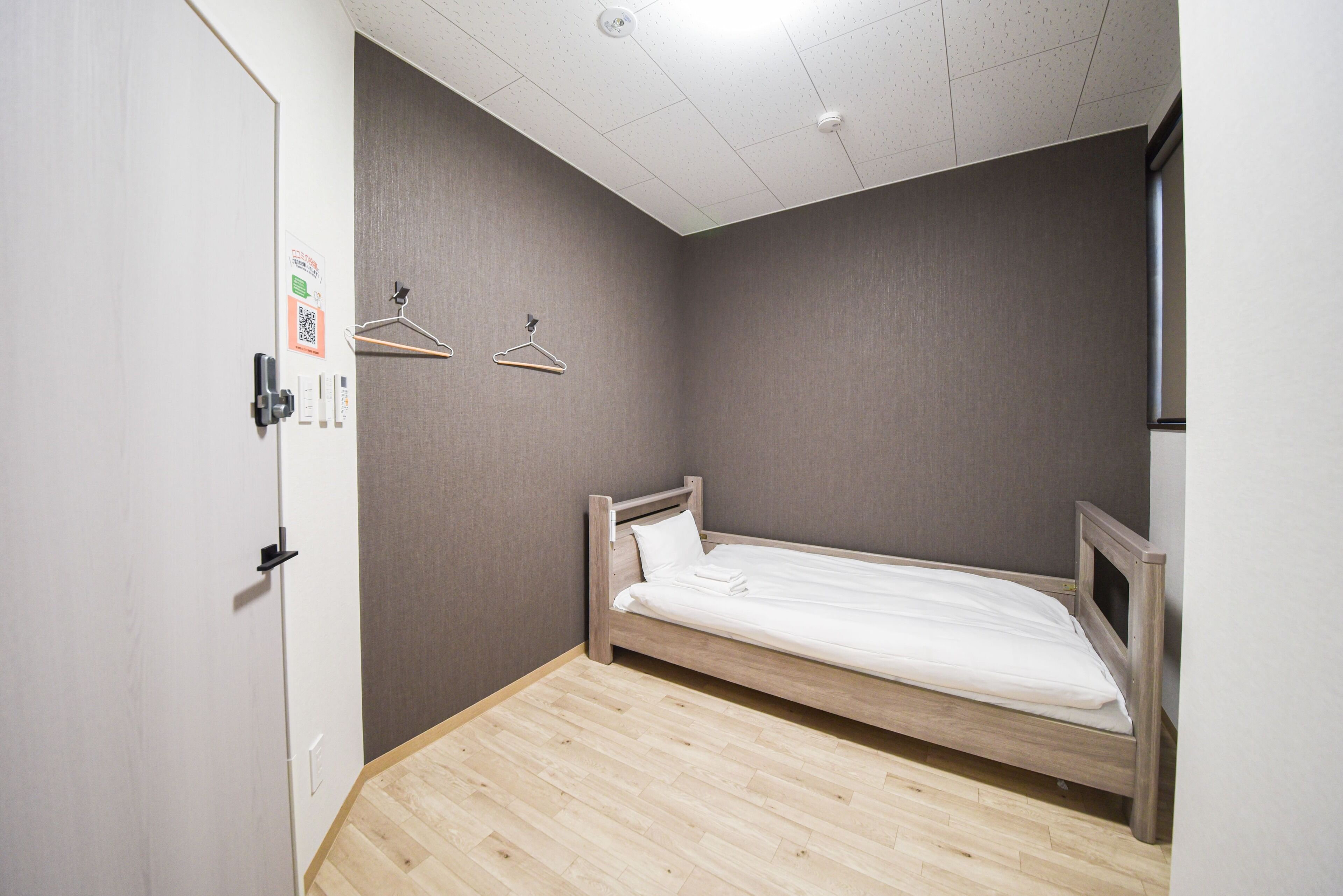 A small, single-bed room with a wooden floor, a grey wall, and a white door.