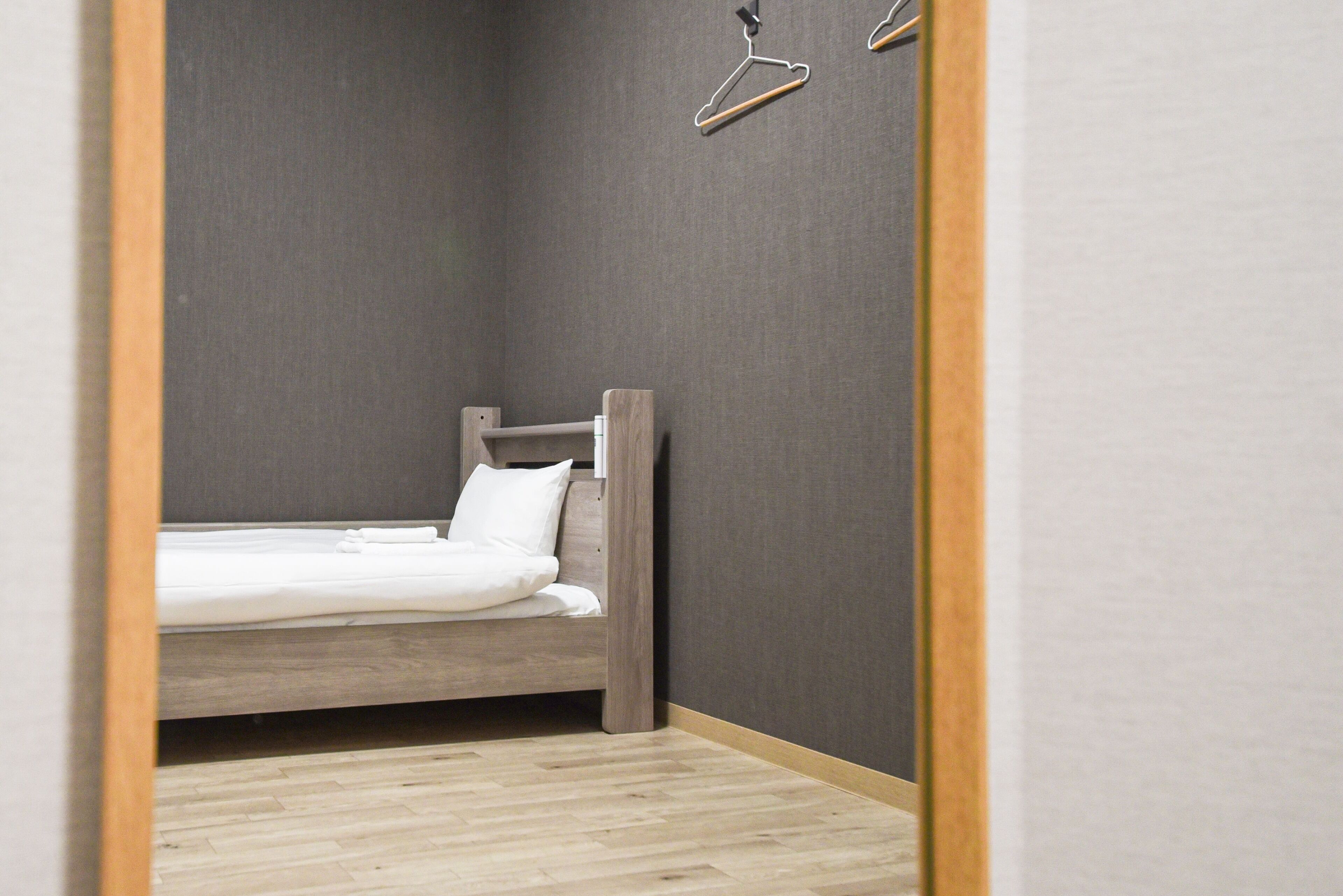 Una habitación pequeña con cama individual, cabecera de madera, paredes grises y piso de madera.