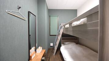 Una habitación de hotel compacta con una litera, un escritorio de madera con una caja de pañuelos, un espejo, un perchero y una puerta.