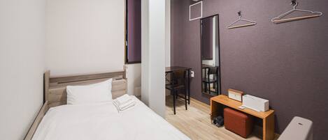 A modern hotel room with a bed, a desk, a chair, and a wardrobe.