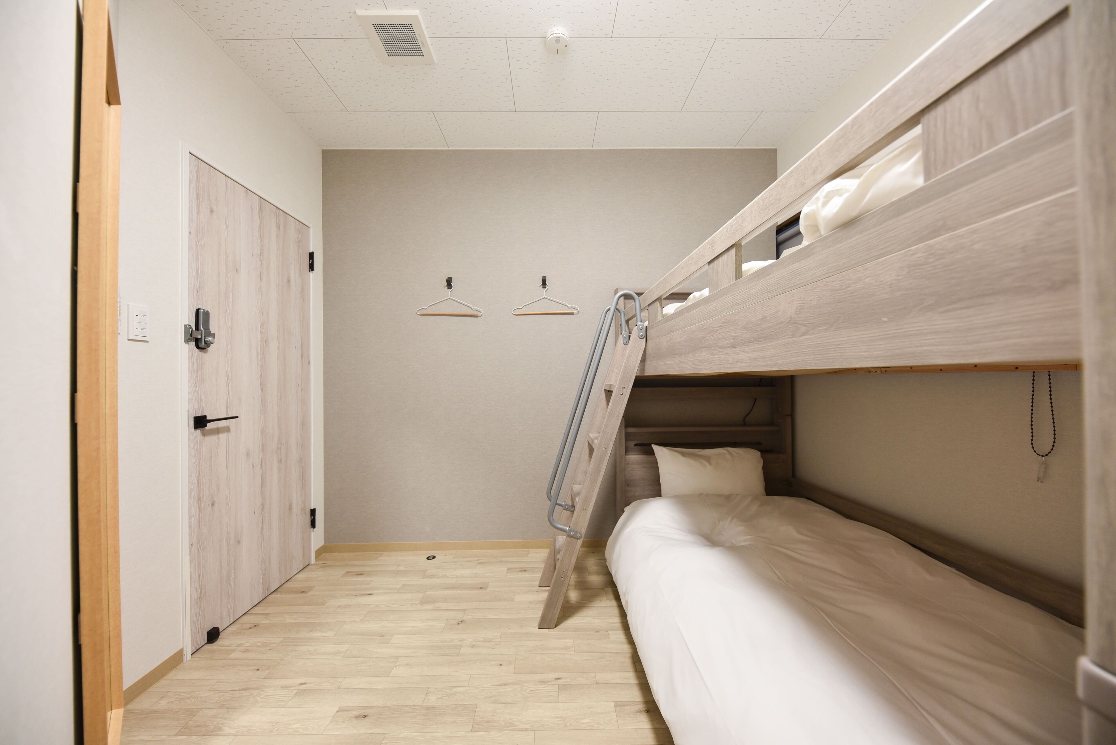 Una habitación de hotel pequeña con una litera, una puerta de madera y piso de color claro.