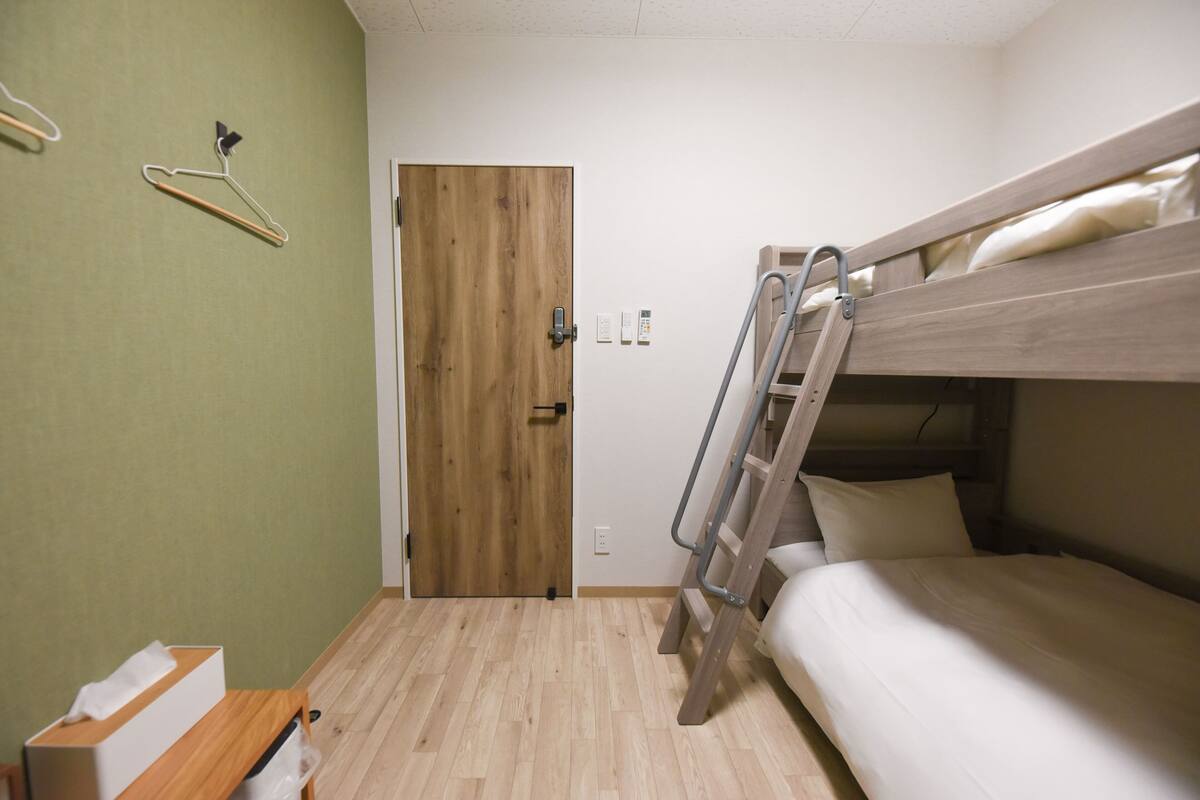 Une pièce avec un lit superposé, une porte en bois, une petite table avec une boîte de mouchoirs et un porte-manteau fixé au mur.