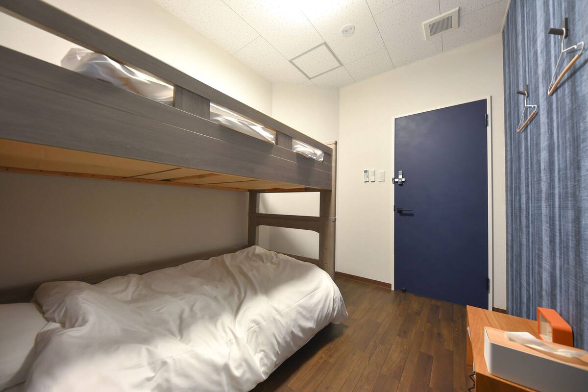 Un lit superposé avec une structure en bois et du linge de lit blanc, une porte avec un rideau bleu et un plancher en bois.