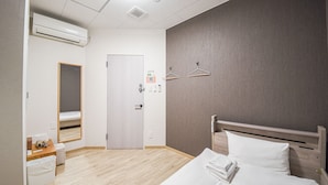 Une chambre d’hôtel avec un lit, un bureau, une chaise, une petite table, un miroir et une porte.