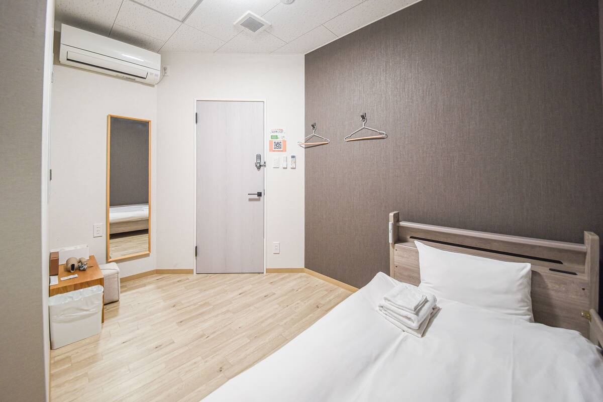 Une chambre d’hôtel avec un lit, un bureau, une chaise, une petite table, un miroir et une porte.