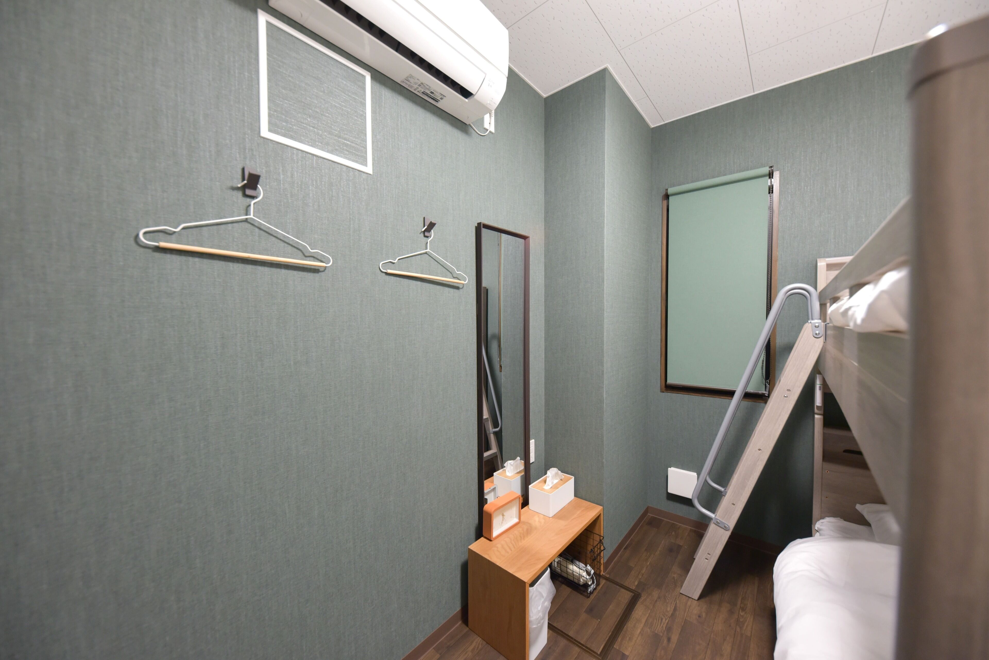 Habitación de hotel con cama, banco de madera, espejo y aire acondicionado instalado en la pared.