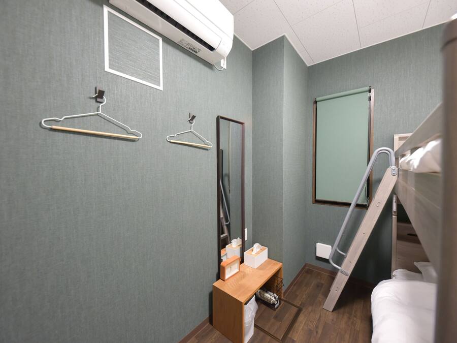 Habitación de hotel con cama, banco de madera, espejo y aire acondicionado instalado en la pared.