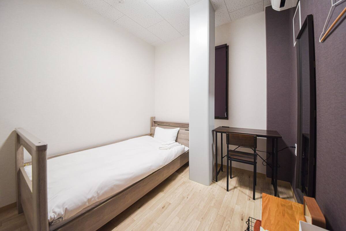 Une petite chambre avec un lit simple, un cadre en bois, un bureau et une chaise.