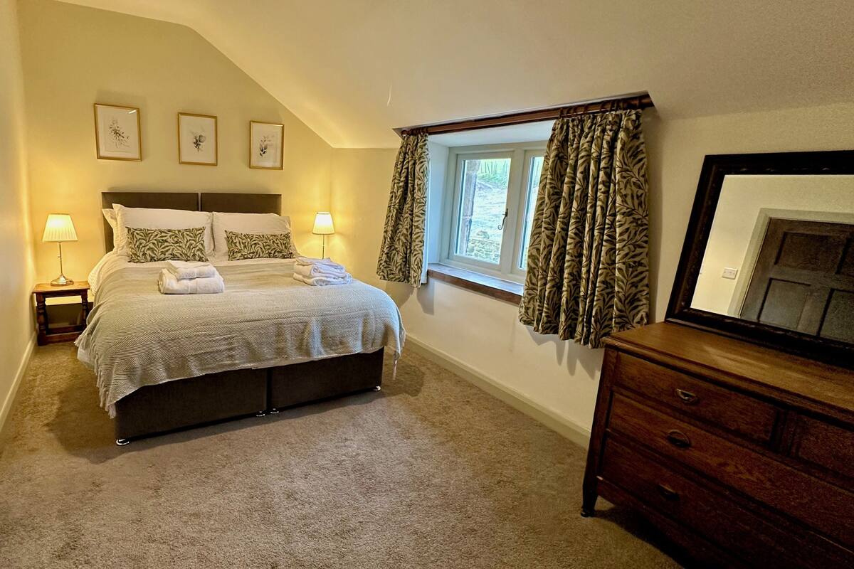Une chambre à coucher comprenant un lit, deux lampes de chevet, une fenêtre avec des rideaux, une commode et trois tableaux encadrés accrochés au mur.