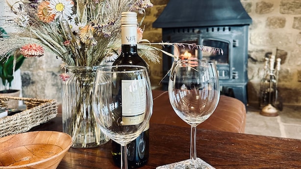 Une table en bois sur laquelle se trouvent une bouteille de vin Pinot Grigio, deux verres à vin et un vase de fleurs séchées.