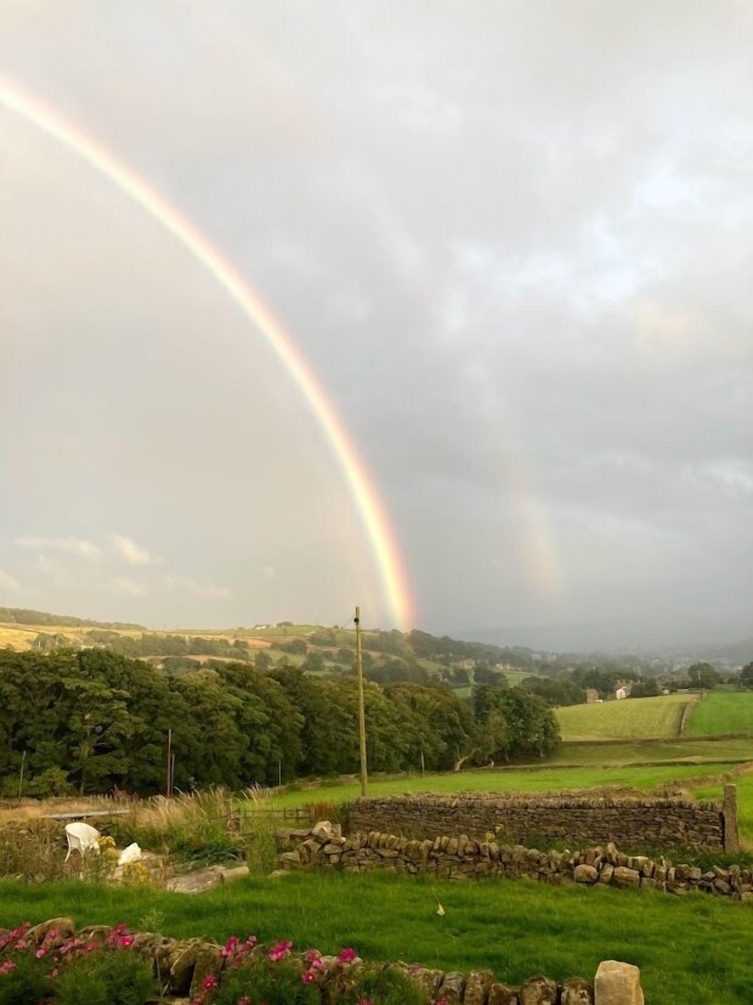 A rural landscape with a stone wall and a rainbow in the sky.